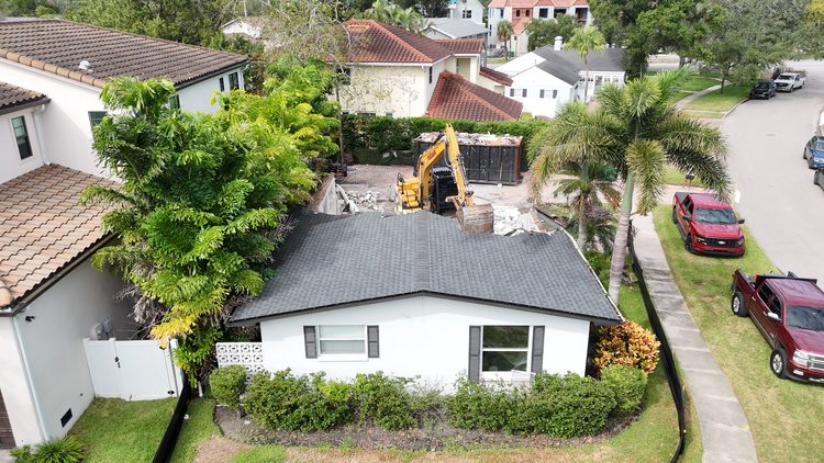 Aerial view of a one-story house on Davis Islands in Tampa before demolition, with an excavator and dumpster behind it