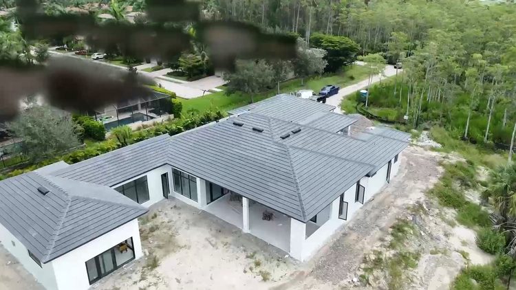 Aerial view of a finished single-story Naples custom home exterior with a gray tile roof and white stucco walls