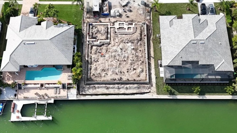 Overhead drone view of a Marco Island canal lot at the foundation stage, between two finished homes