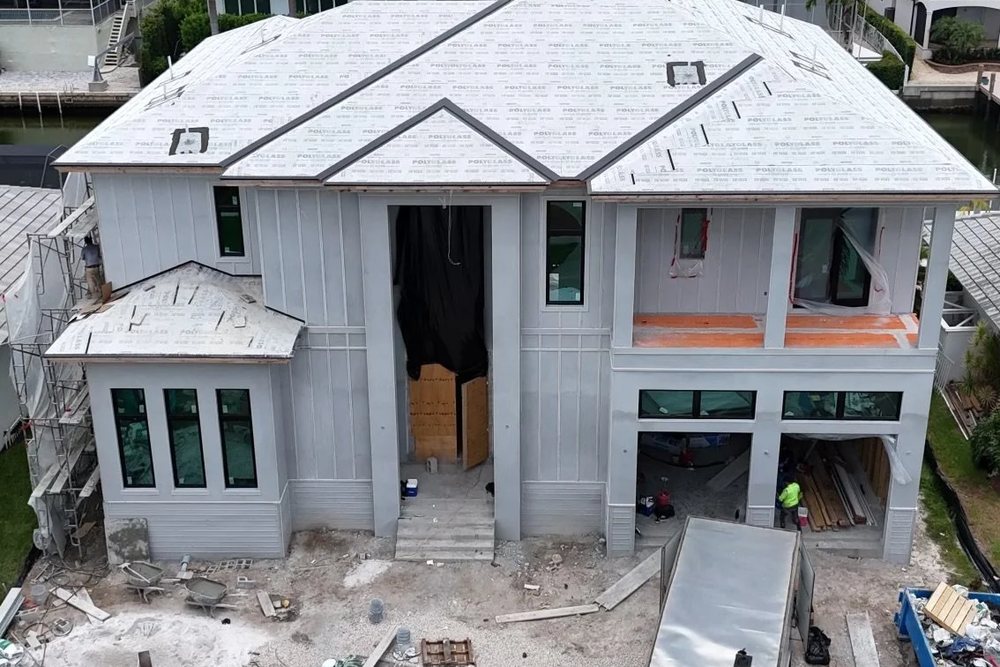 Two-story custom home under construction on a Marco Island canal, with windows installed, roof underlayment down and a raised front entry
