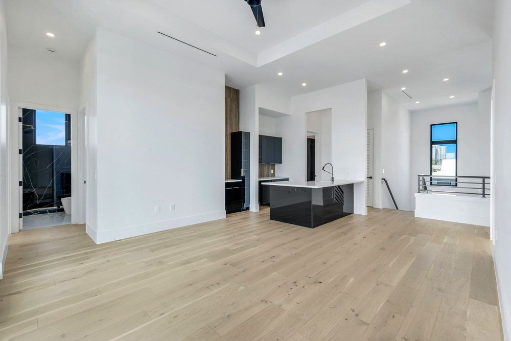 Open upstairs loft with a black wet bar, wide-plank wood floors and white walls in a contemporary Marco Island custom home