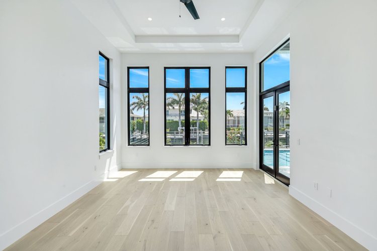 Bright bedroom with tall black-framed windows and glass doors opening to a pool, with a Marco Island canal beyond